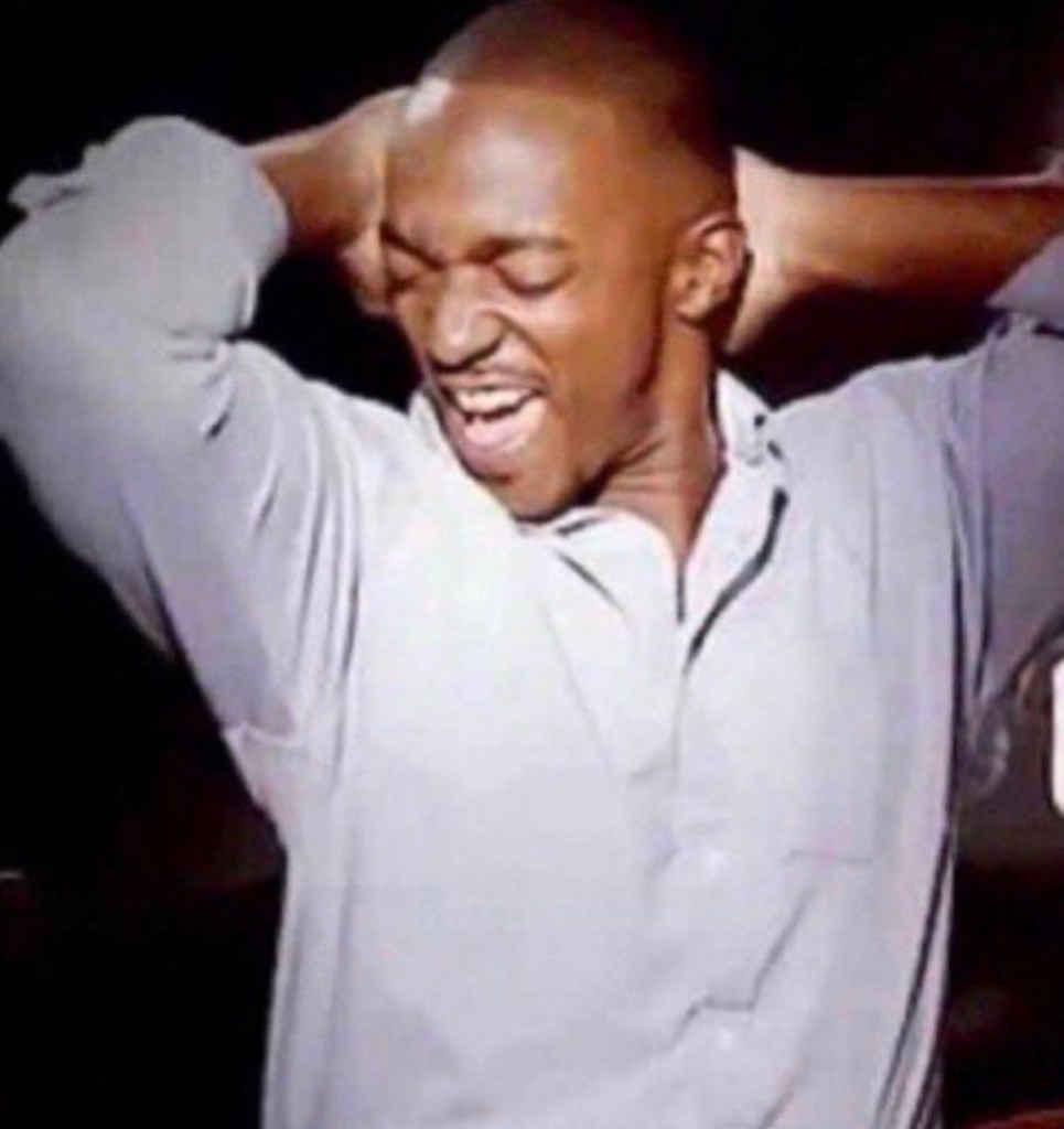 A man expressing excitement or joy, with his hands behind his head and a wide smile on his face.
